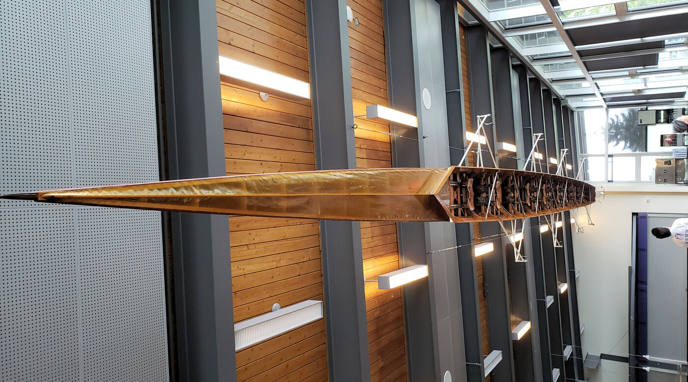 The Husky Clipper, the eight-oar shell George Pocock built for the University of Washington crew that won gold in Berlin in 1936, hanging in the Conibear Shellhouse in Seattle. Photo by AdmiralHts, CC BY-SA 4.0, via Wikimedia Commons.